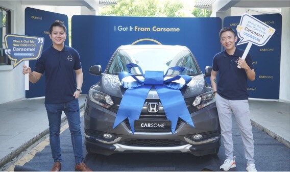 Founders holding CARSOME buy car signage with a car wrapped in blue ribbon in between